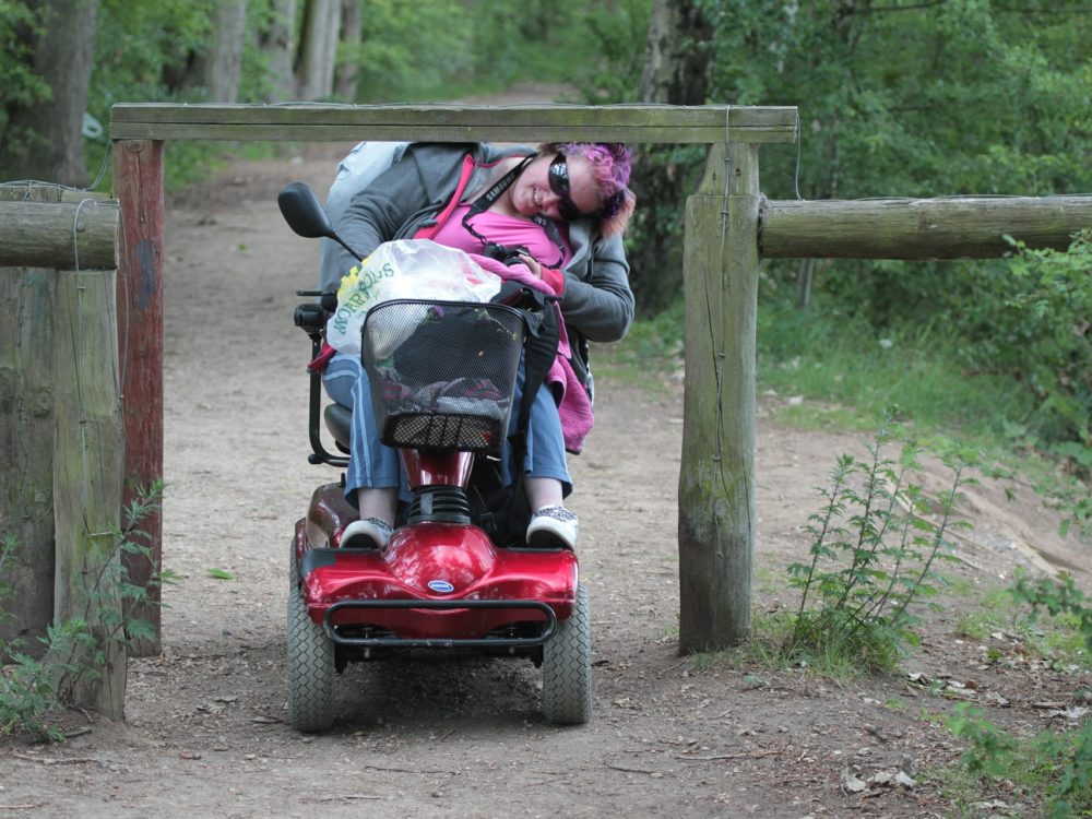 Wheelchair user attempting to enter a dirt trail through an inaccessible gate