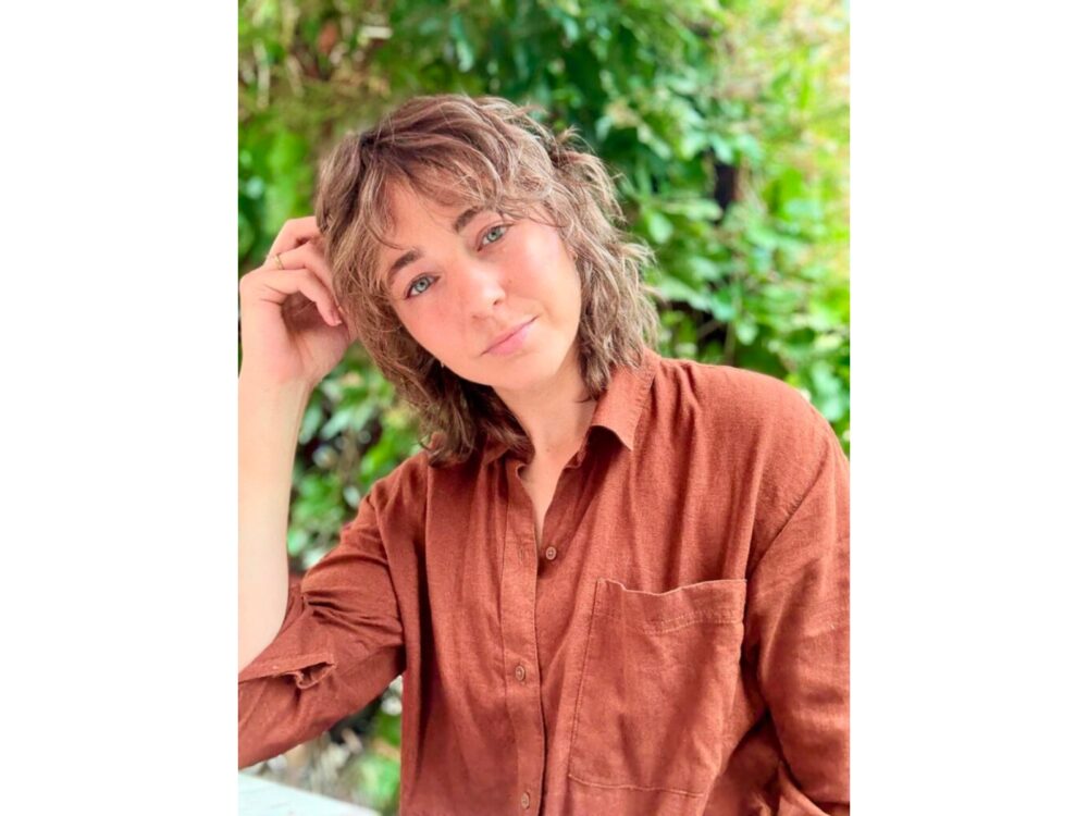 A portrait of Beth Wittmann smiling near summer foliage.