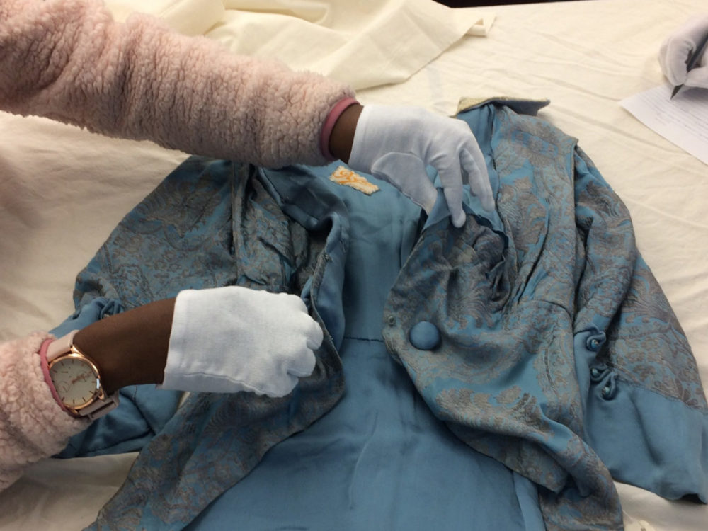 Researchers work on a blue ensemble while wearing white gloves