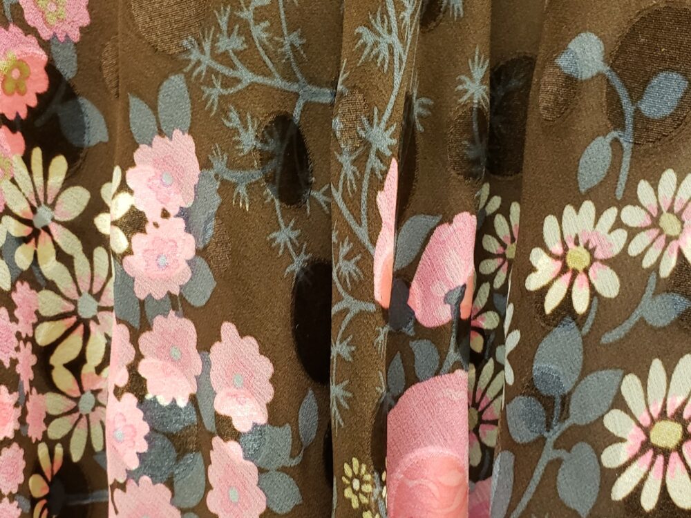 Detail of fabric with brown background and pink and white flowers on display in the Richard Blackwell Gallery