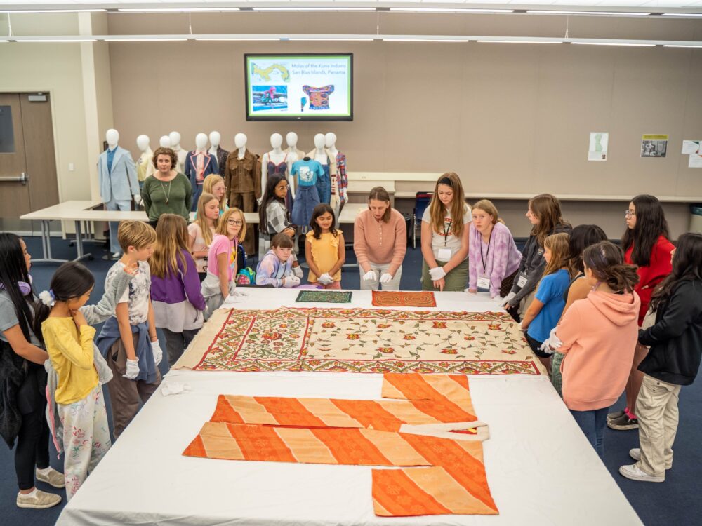 A large group of students gather to look at garments laid on a table in the Avenir classroom, one of their educational spaces.