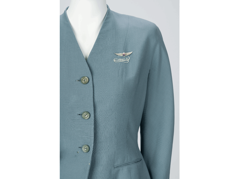 A detail image of a blue flight attendants uniform with a pin on the breast.