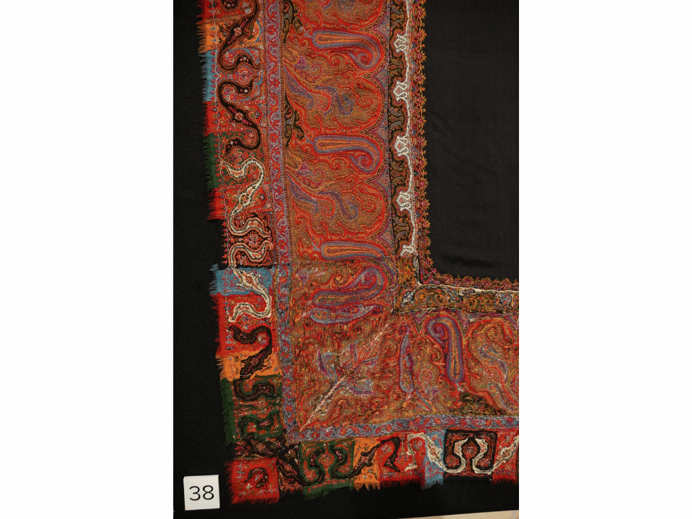 A detail view of the corner of a large paisley shawl in a museum exhibition.