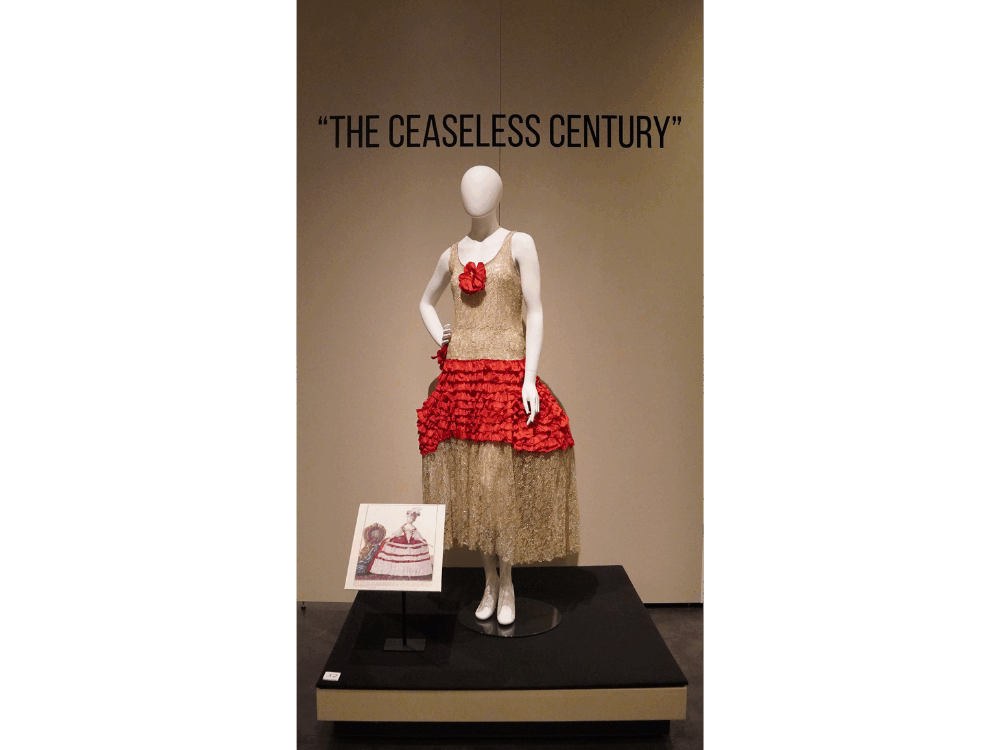 An installation view of a robe de style made of metallic gold lace with bright red ruffles at the waistline.