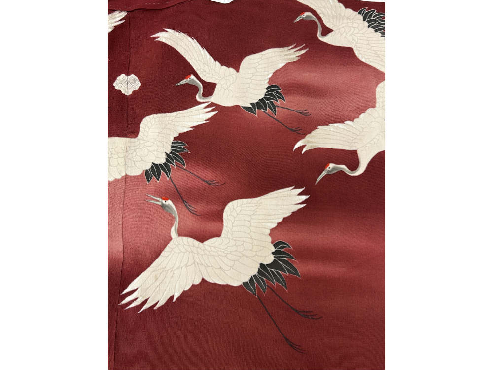 A detail image of a Japanese kimono. The kimono is red with white cranes flying.