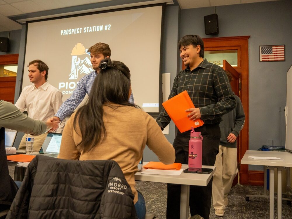 Students shake hands with industry partners and mentors in a classroom.