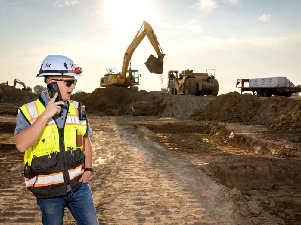 A construction management student stands on dirt during a construction dig while wearing construction equipment.
