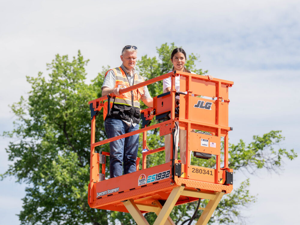 A young woman and a CSU Construction Management industry partner smile while operating a forklift.