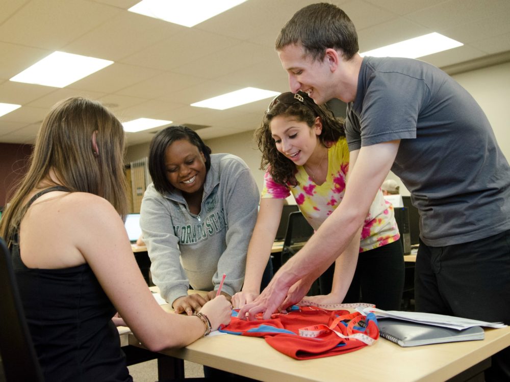 A group of students in our programs and degrees gather around a garment to take measurements for a technical package in a product development course.