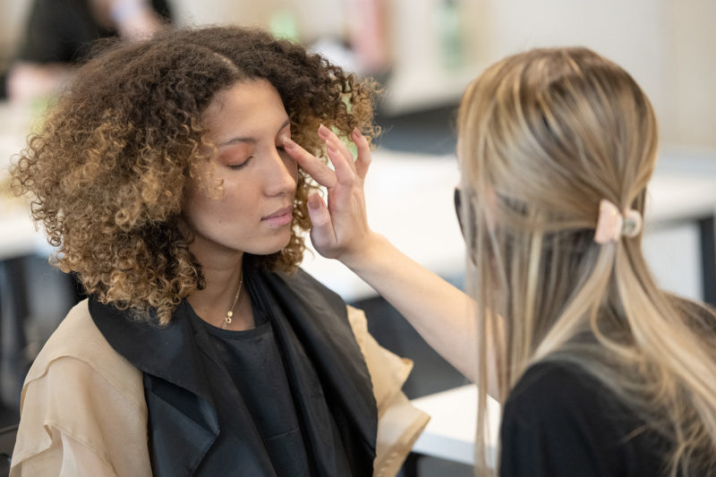 A student applies make-up to a model