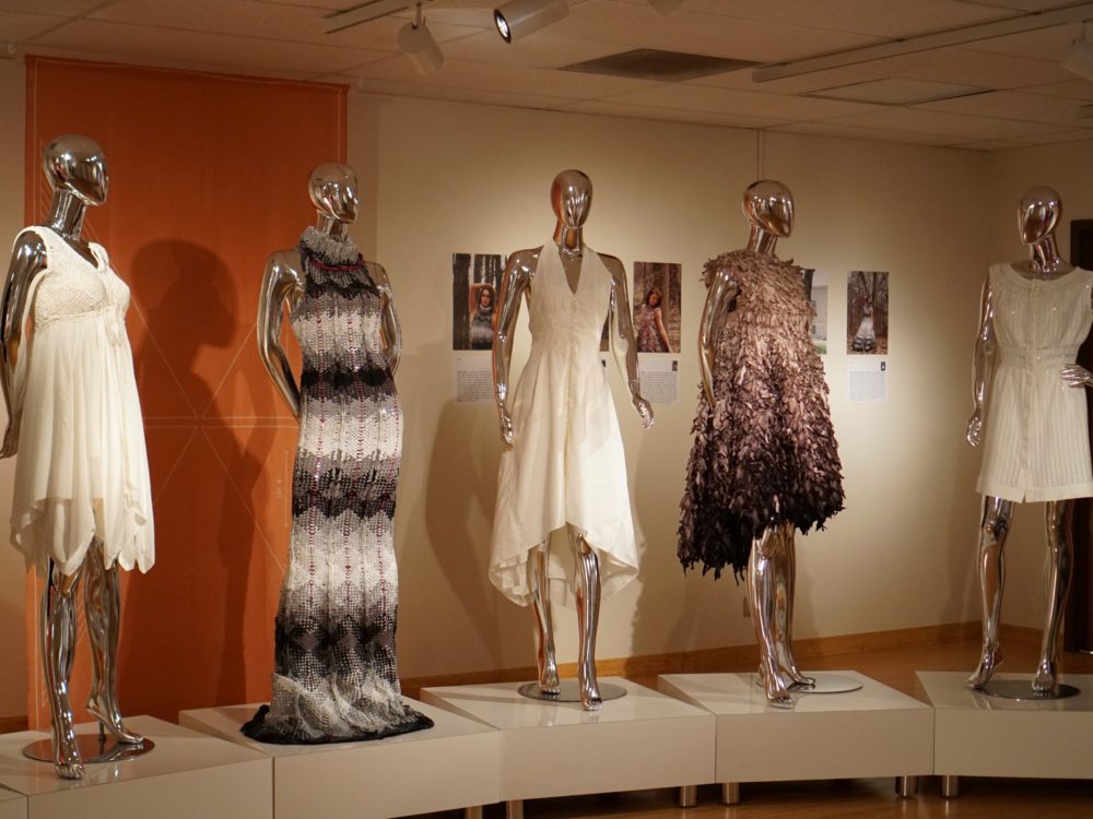 Five mannequins outfitted in intricate gowns fill a gallery space.