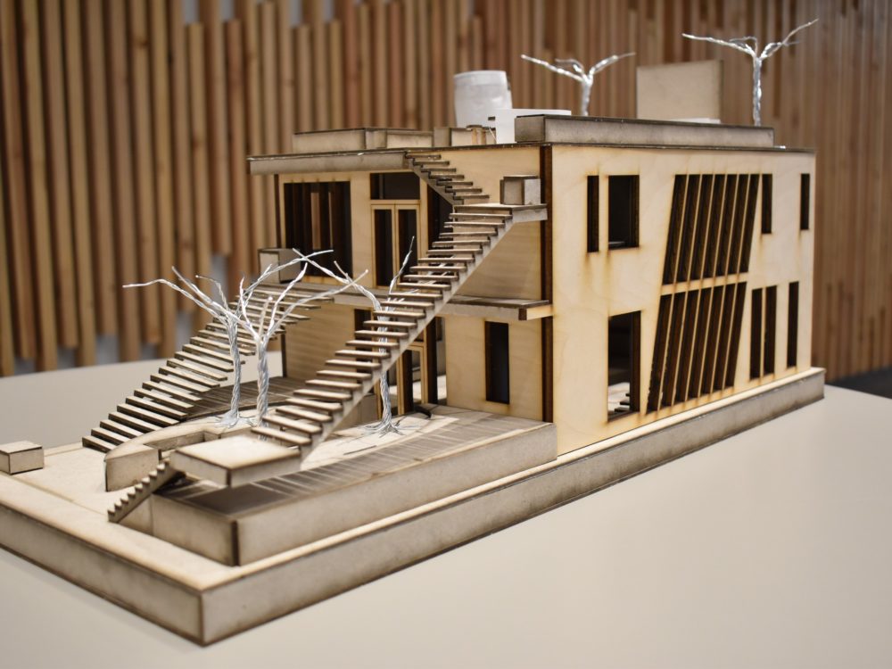 A building model constructed with sood and wire and featuring intricate staircases and windows sits on a table .