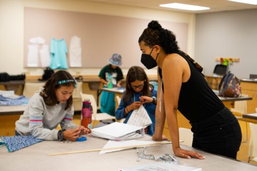 Students learn how to pin fabric from a teacher