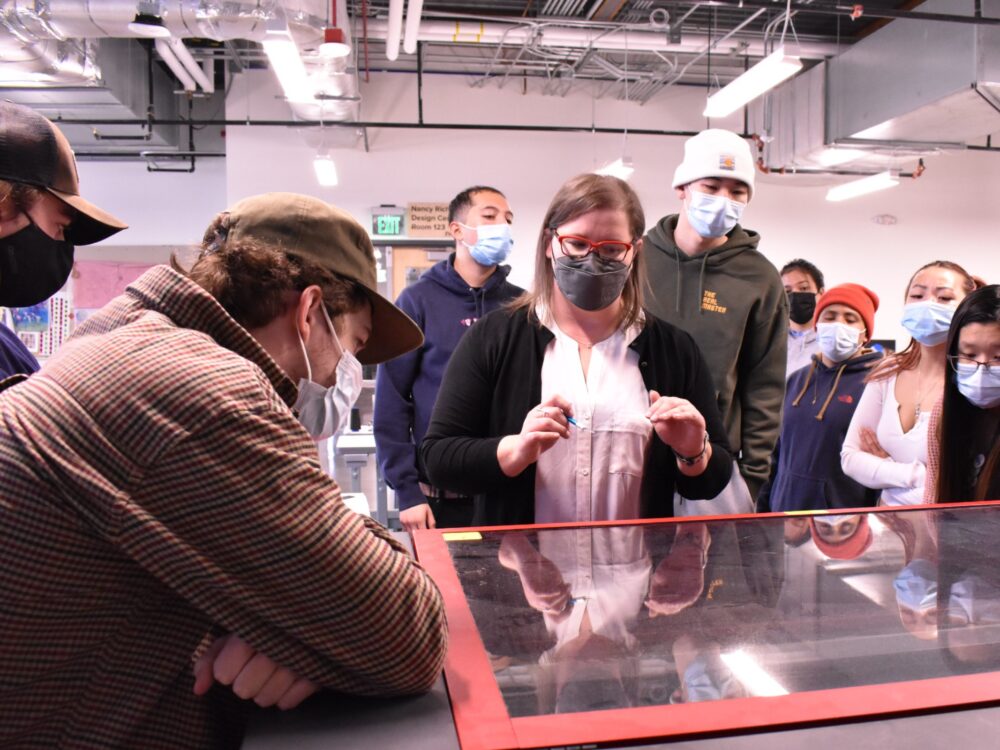 Students gather around the industrial laser cutter