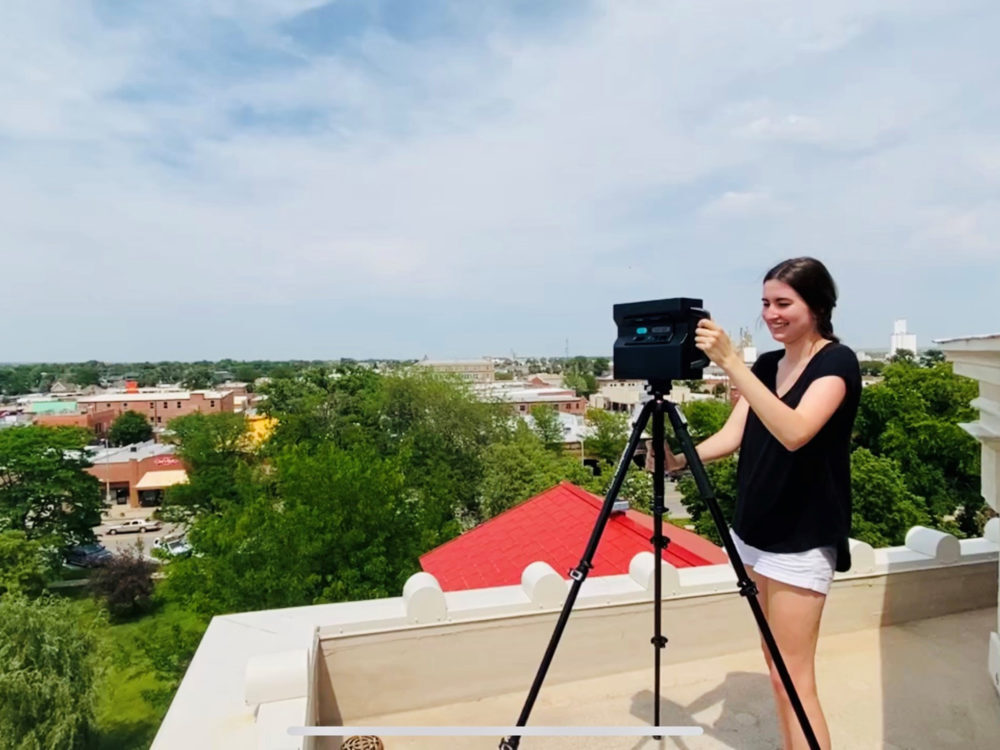 Sara Bovaird stands atop a building in Sterling with a 3D camera documenting historic architecture