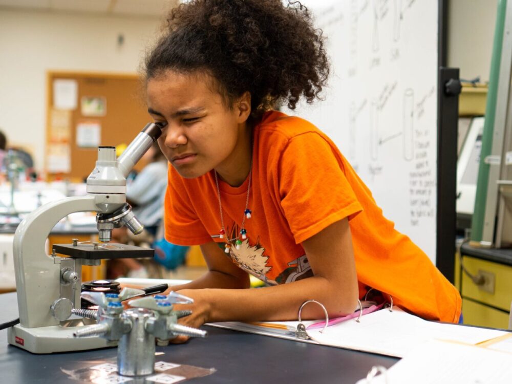 A middle school student looks through a microscope in a textile science lab