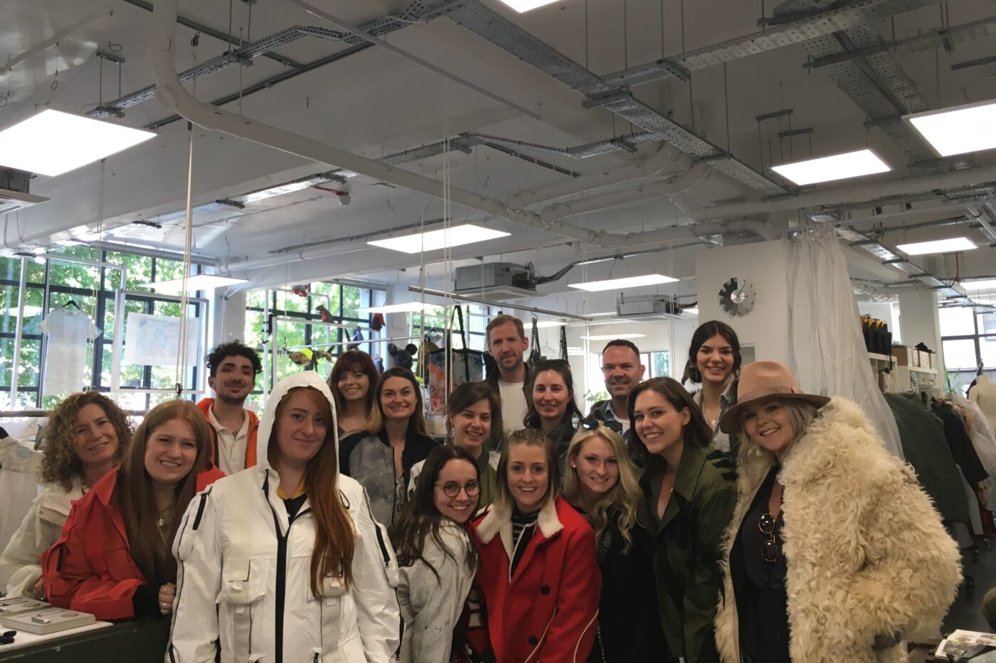 A large group of students and two faculty members stand in a London clothing workshop
