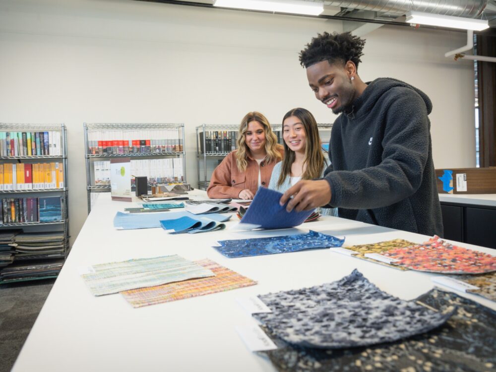 three students look at textile materials for interiors in the design library.