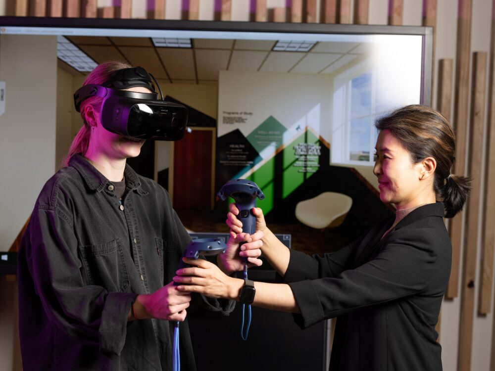 a faculty instructor aids a student with a virtual reality headset in interior design.