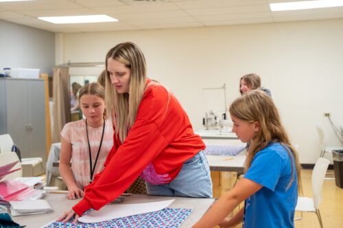 two students get help from a teacher measuring out on fabric