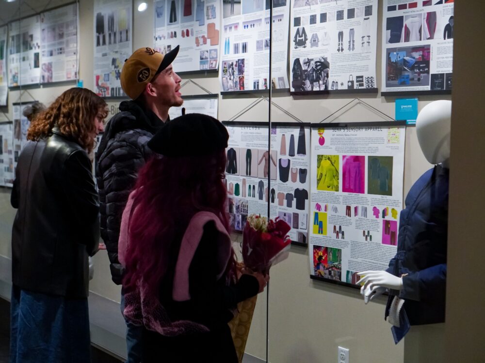 3 people look at poster displays on adaptive apparel as part of the research in the Inclusive Innovations Laboratory