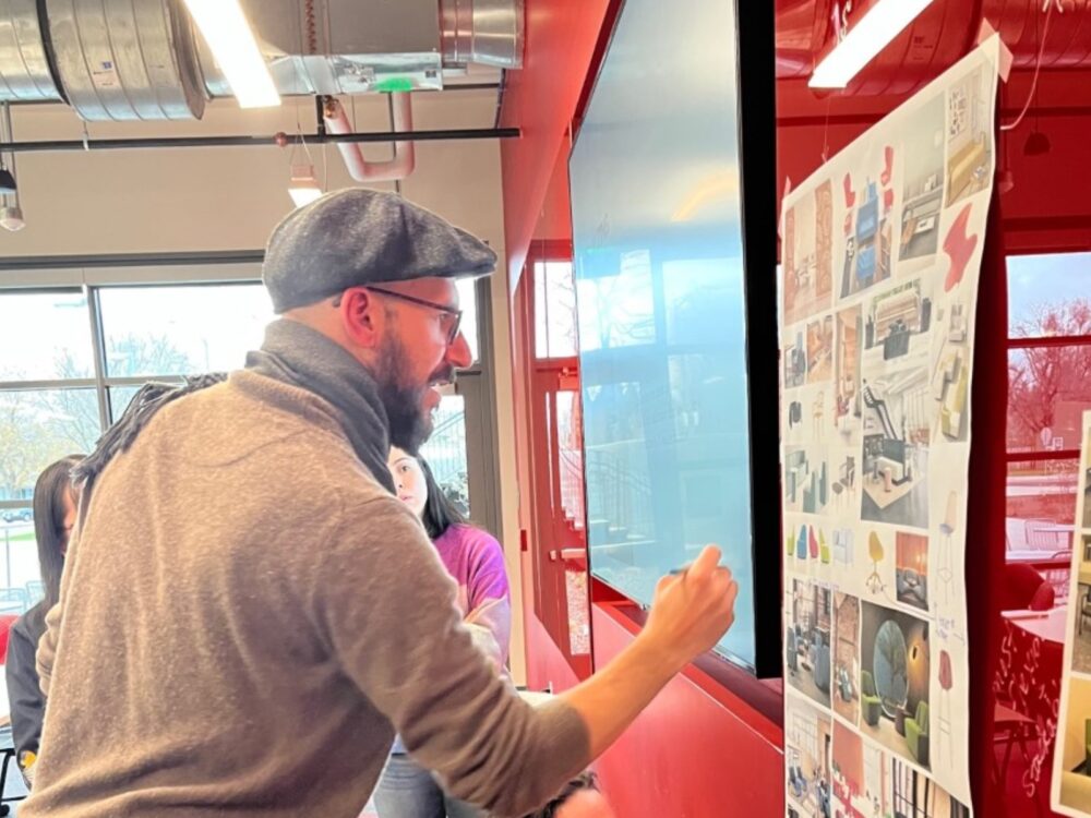2 people work on providing feedback on a poster mounted on a red wall