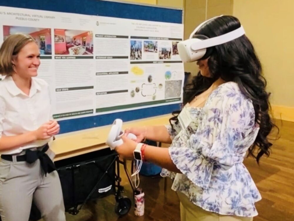 Amandap Spitzer presenting her research poster with a guest trying out the virtual reality headset.