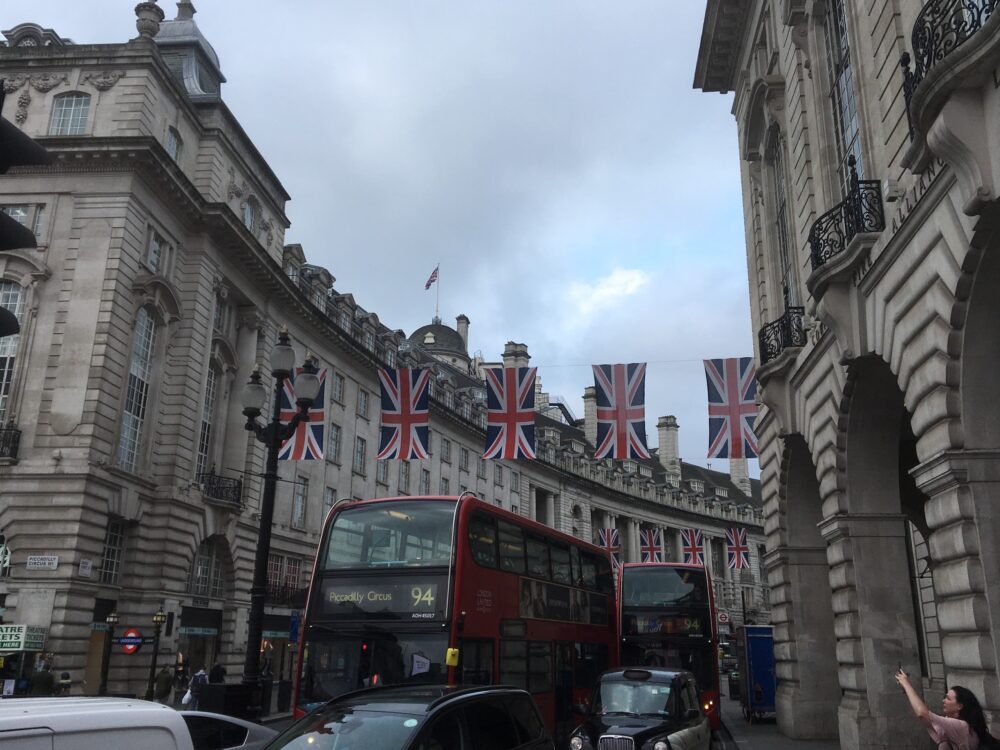 buildings in london with british flags above a red double decker bus