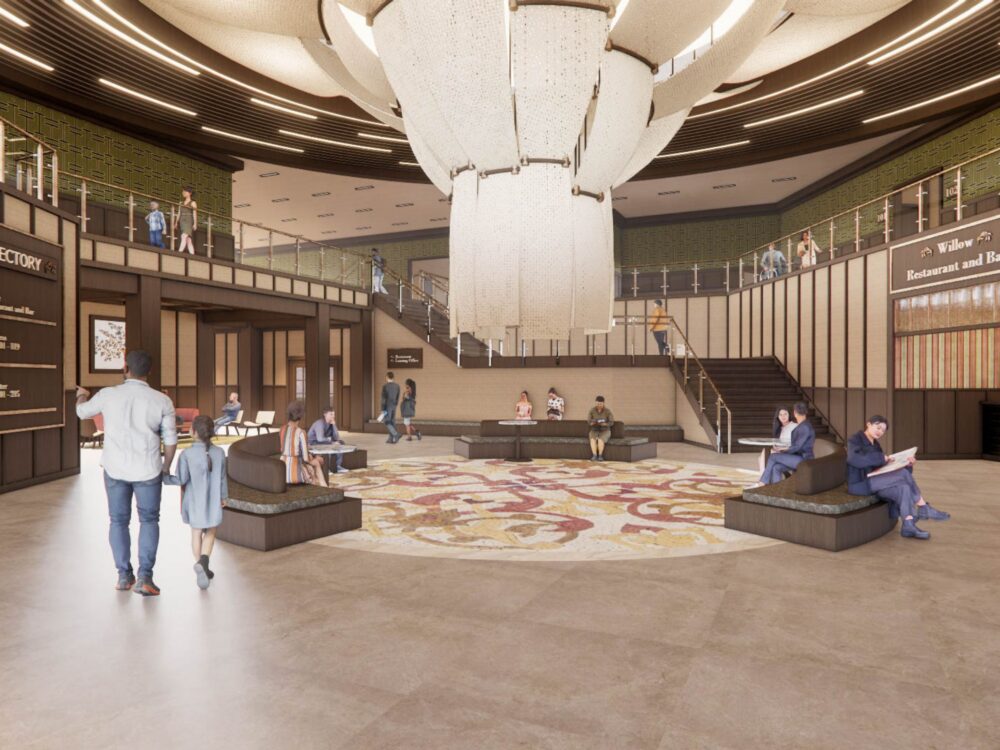 A grand hotel‑style lobby with a massive central chandelier, patterned rug, tiered seating, directory signage, and access to upper levels via stairs and balconies.