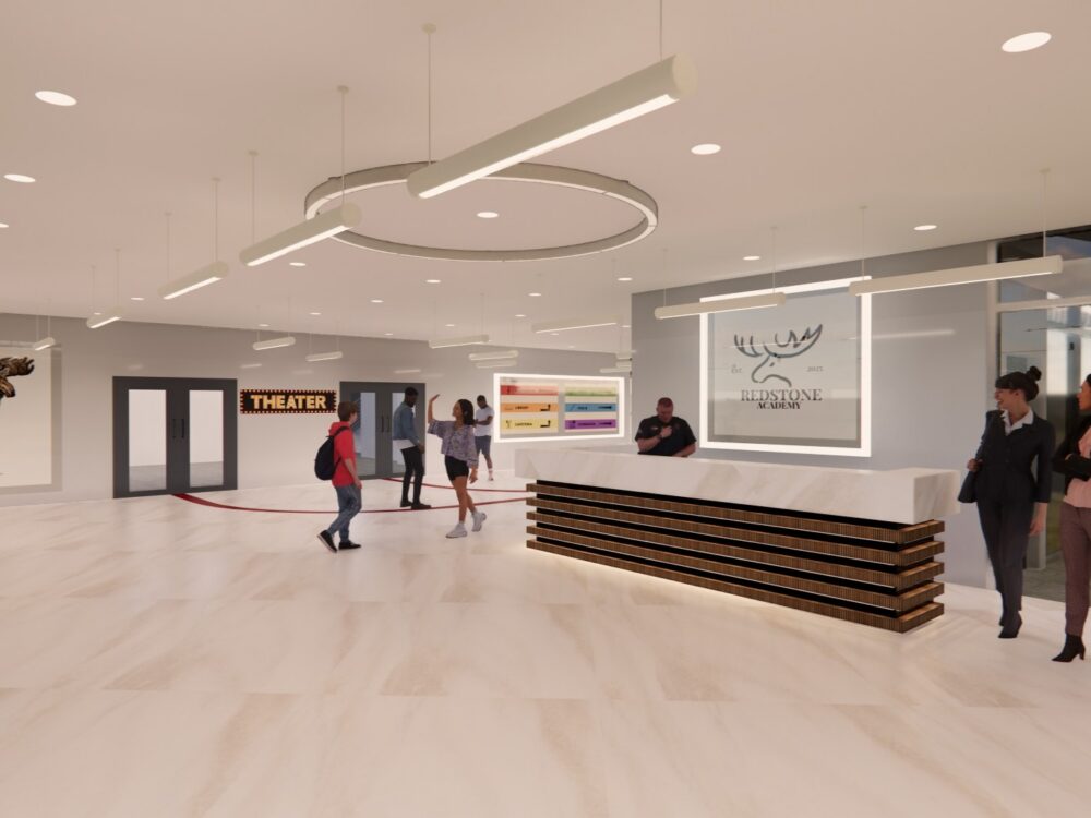 A bright, contemporary lobby with a long reception desk, illuminated signage, directional theater entrance, and people moving through the open space.