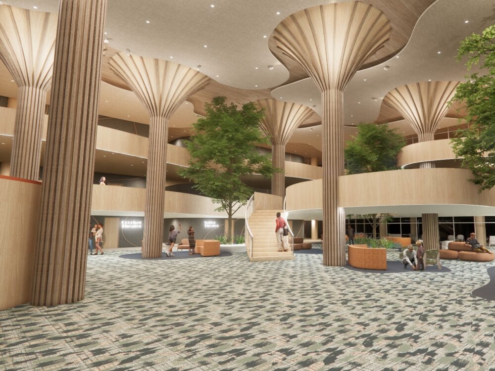 A large open lobby with flared column structures, indoor trees, patterned carpeting, and tiered balcony levels surrounding flexible seating zones.