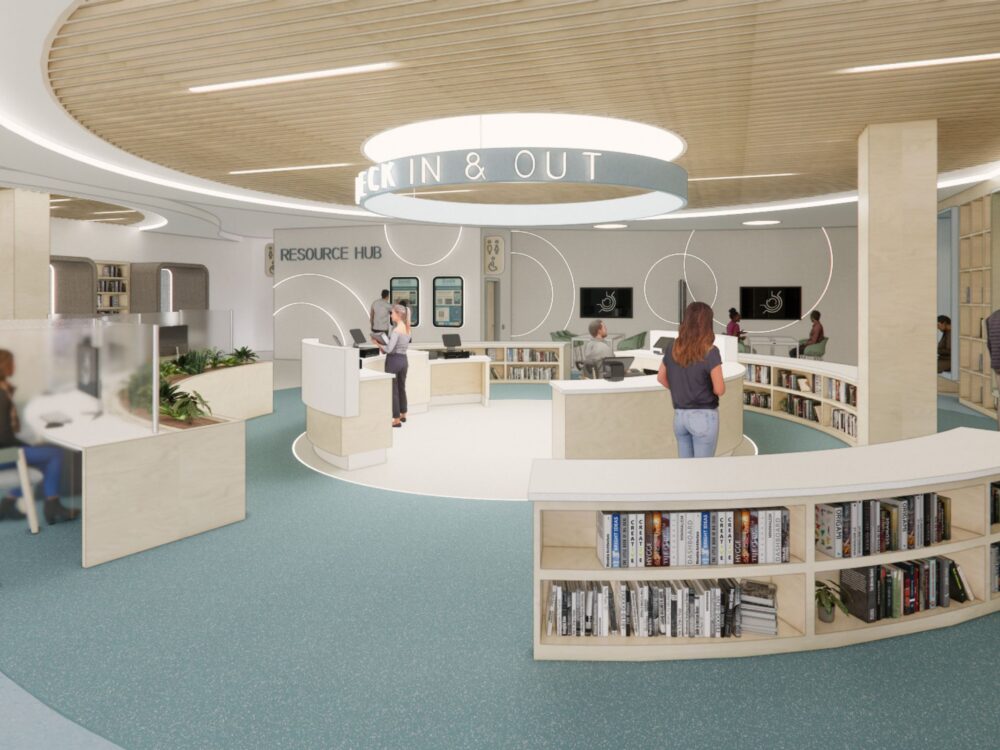 A circular library check‑in hub with curved bookshelves, wood-paneled ceiling, digital screens, and multiple staffed stations beneath a large overhead sign.