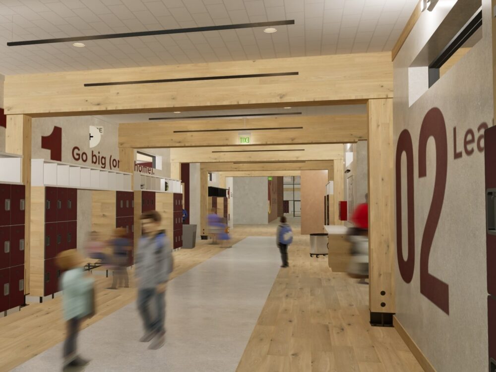 A school corridor with wood beams, bold numbered graphics, red lockers, and students moving through the wide, open hallway.