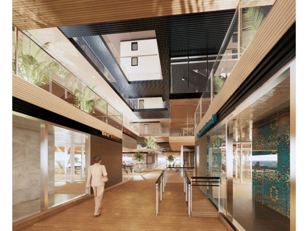 Interior rendering of a modern commercial corridor with wood ceilings, glass storefronts, and patterned wall panels. Natural light enters from above through a large central atrium. Planters with greenery line upper levels, and signage for various retailers is visible along the walkway. A person in business attire walks through the corridor toward an open plaza area.