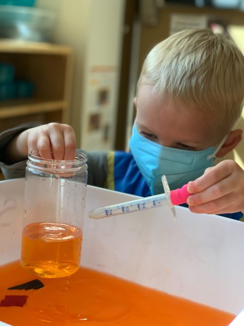 Boy playing with a jar of orange liquid and an eyedropper