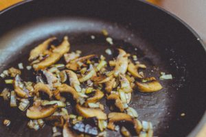 Mushrooms being sauteed in a pan with onions