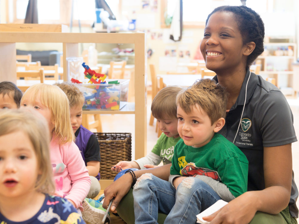 An early childhood education employee sits with toddlers in a classroom.