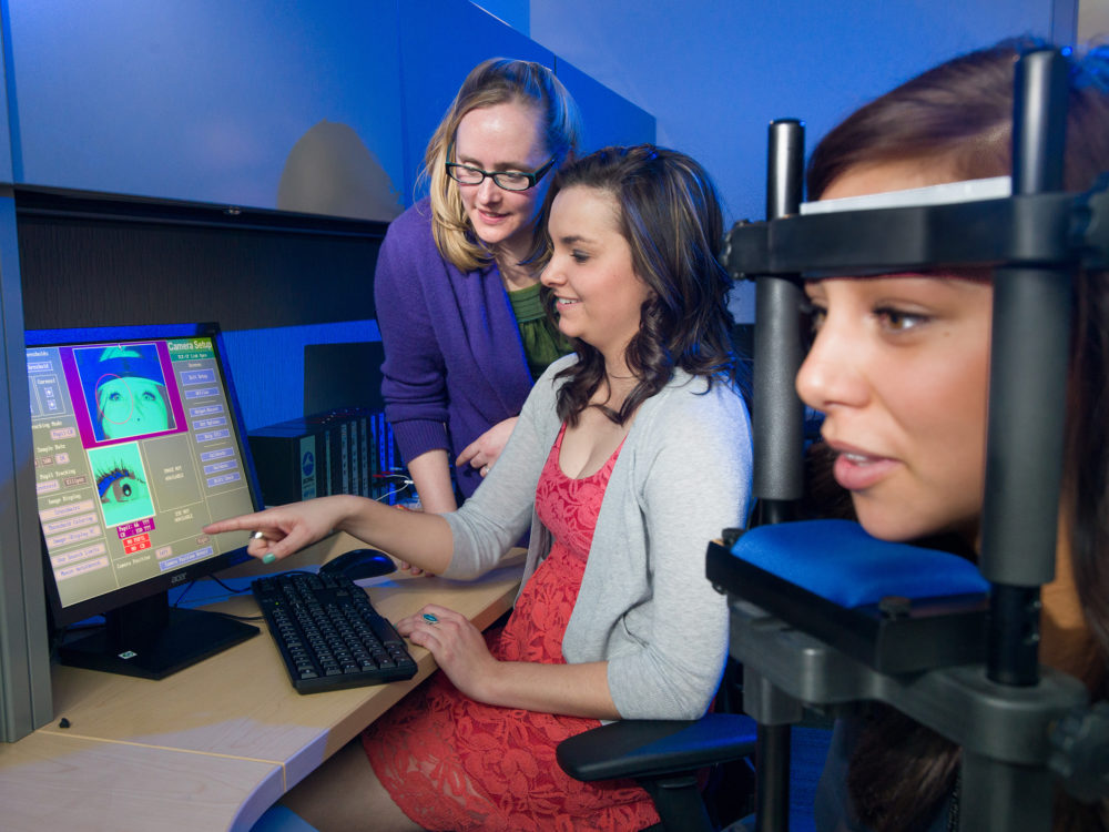 Laura Ferrare and Dr. Rachel Graham Lucas-Thompson consult as Madison Lampe volunteers for an eye-tracking research project in Lucas-Thompson's lab.