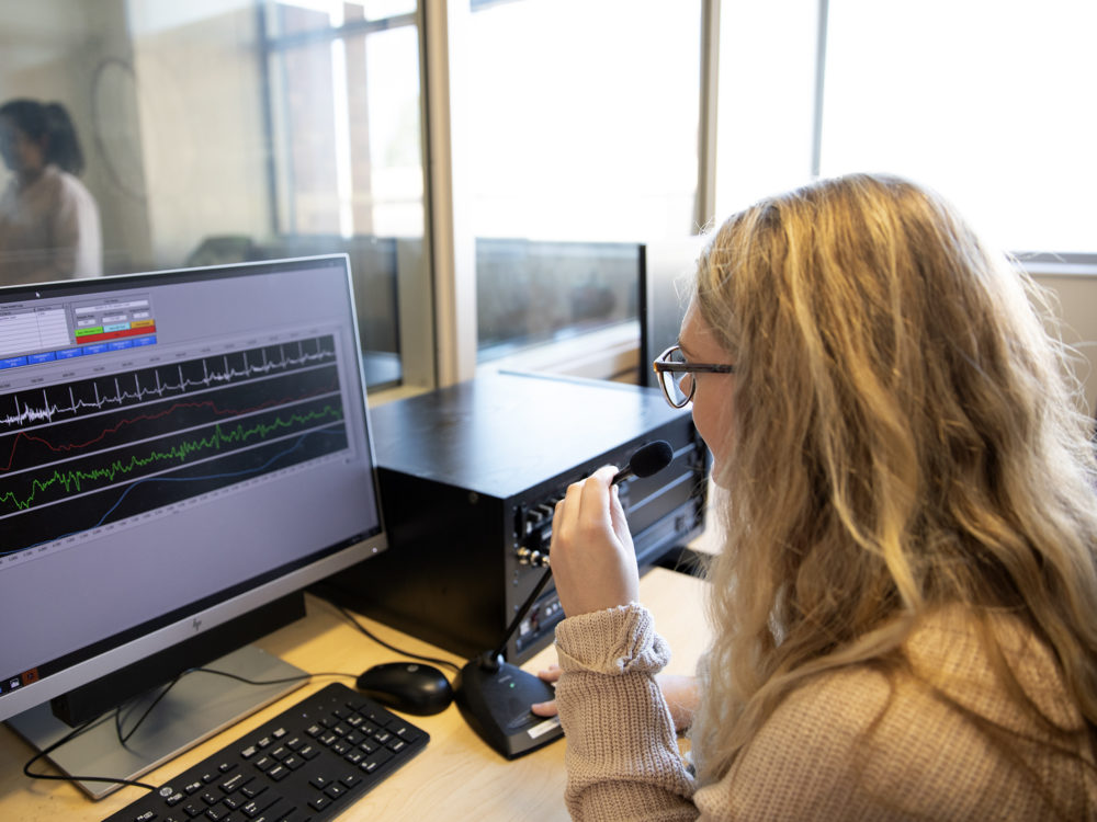 A researcher looks at study participants through glass partition.