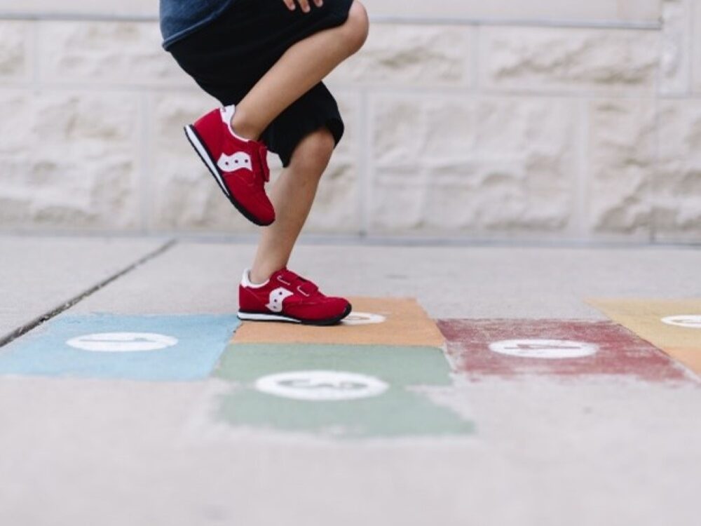 Person wearing red shoes playing hopscotch on colorful squares.