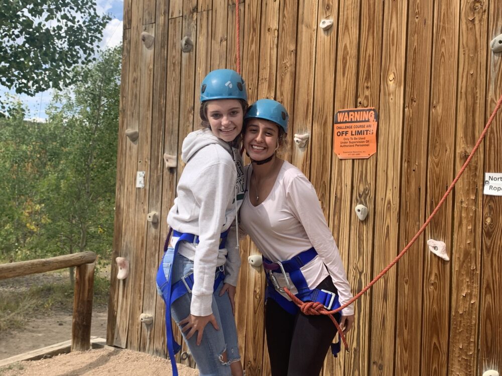 Two individuals smile in front of rock climbing wall.