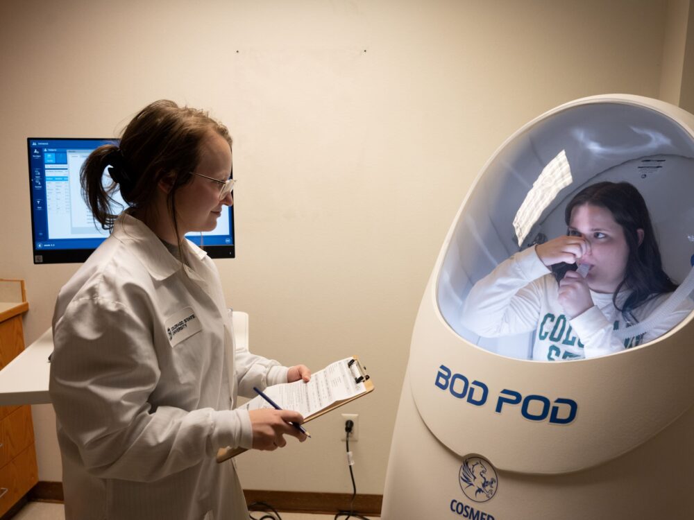 Person in lab coat oversees participant in human-sized pod.