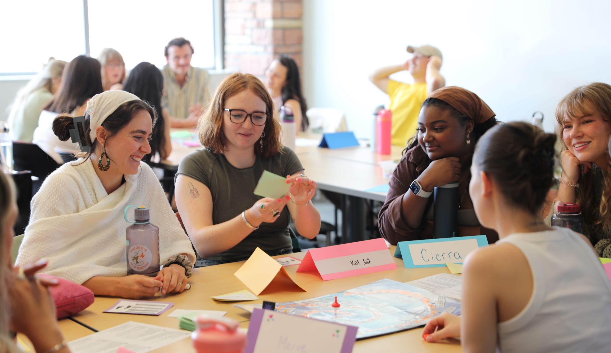 A group of students play a board came and smile while looking at a playing card.