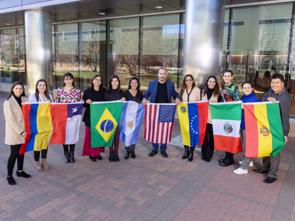 A group of Developmental Disabilities Lab members and collaborators smile while holding various international flags.