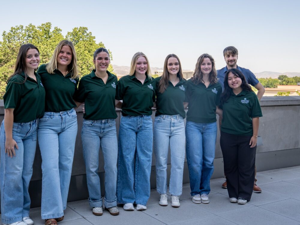 A group of CSU Human Development and Family Studies peer advisers smile at CSU's Behavioral Sciences Building
