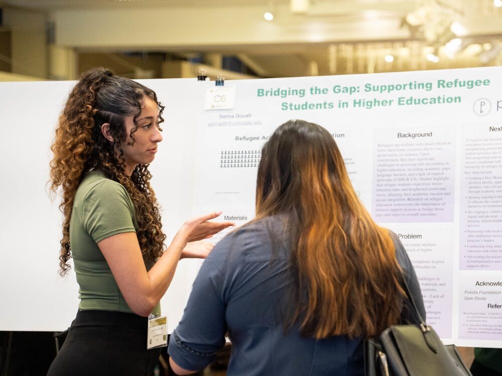 An undergraduate researcher smiles while presenting her research poster to a guest judge.