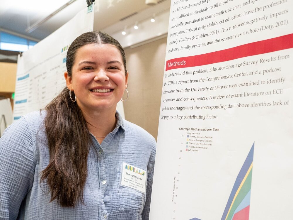 An undergraduate researcher smiles next to her research poster at a showcase event.