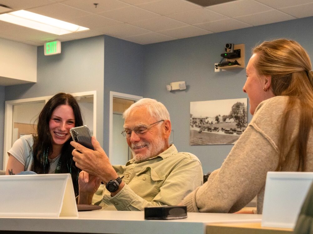 CSU students and an older adult community member smile while conversing with each other.