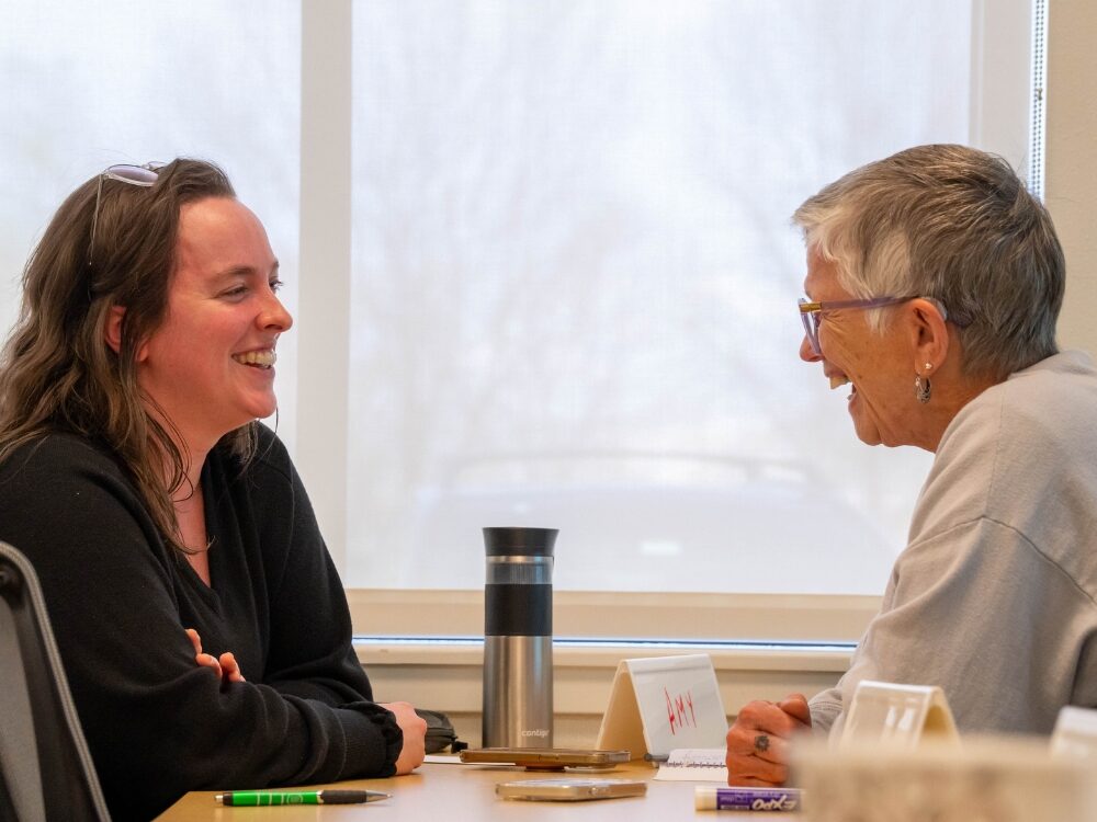 A CSU student and an older adult community member smile while conversing with each other.