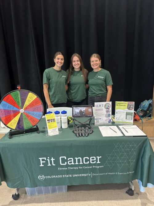 Three members of the PATP Lab team smile while tabling at an event. The Table has a prize wheel and conference swag, and the table reads 